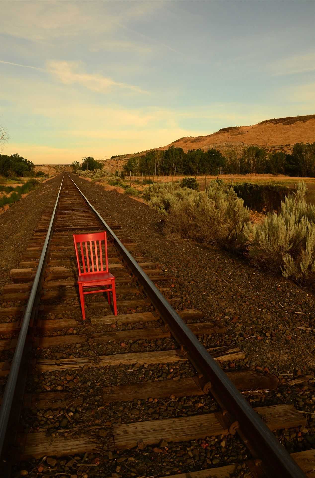 Red chair put on a railroad tie in the middle of the tracks as they go off into the distance