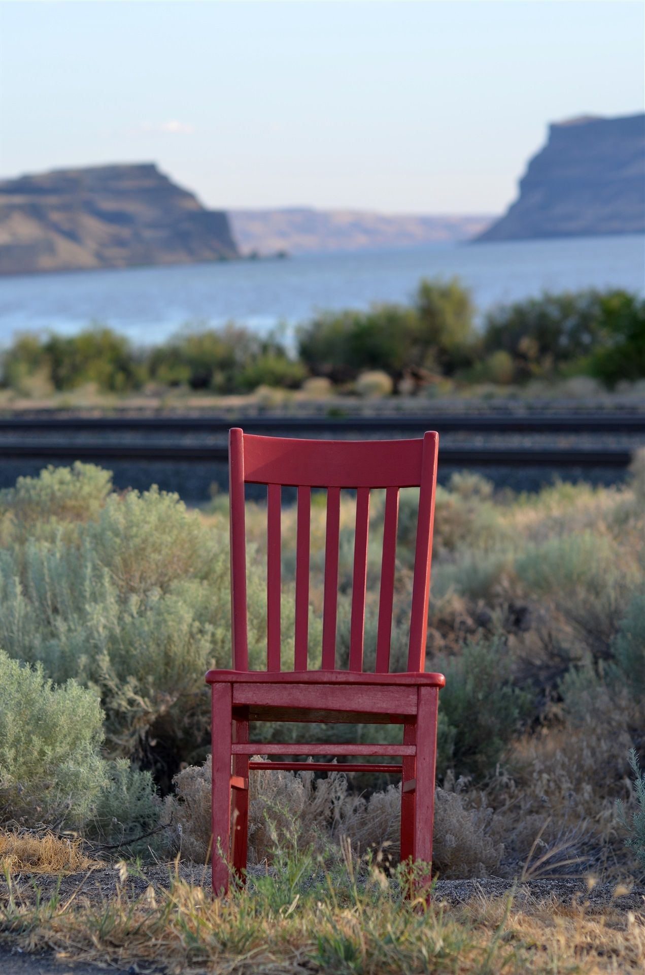 Red chair sitting amongst some brush with the bay and cliffsides in the background