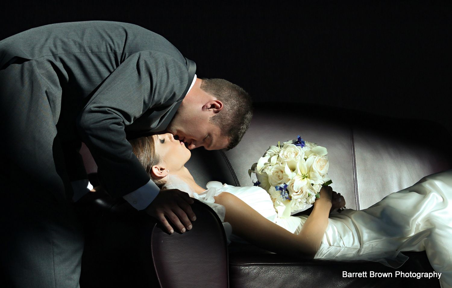 Groom kissing bride as she lies on a couch like Sleeping Beauty