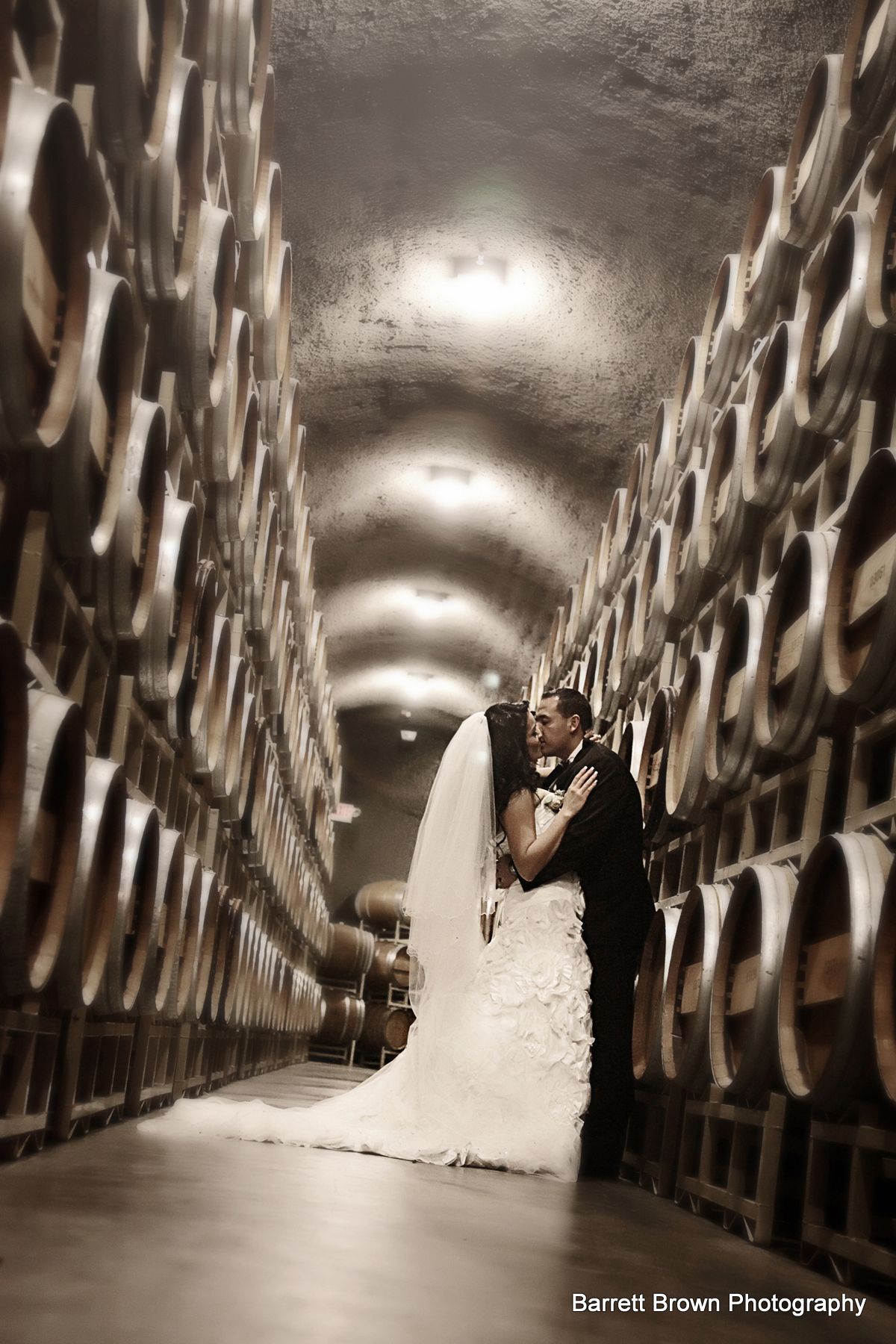 Groom dipping bride while the couple kiss in a warehouse between two four-barrel high alcohol fermentation barrels