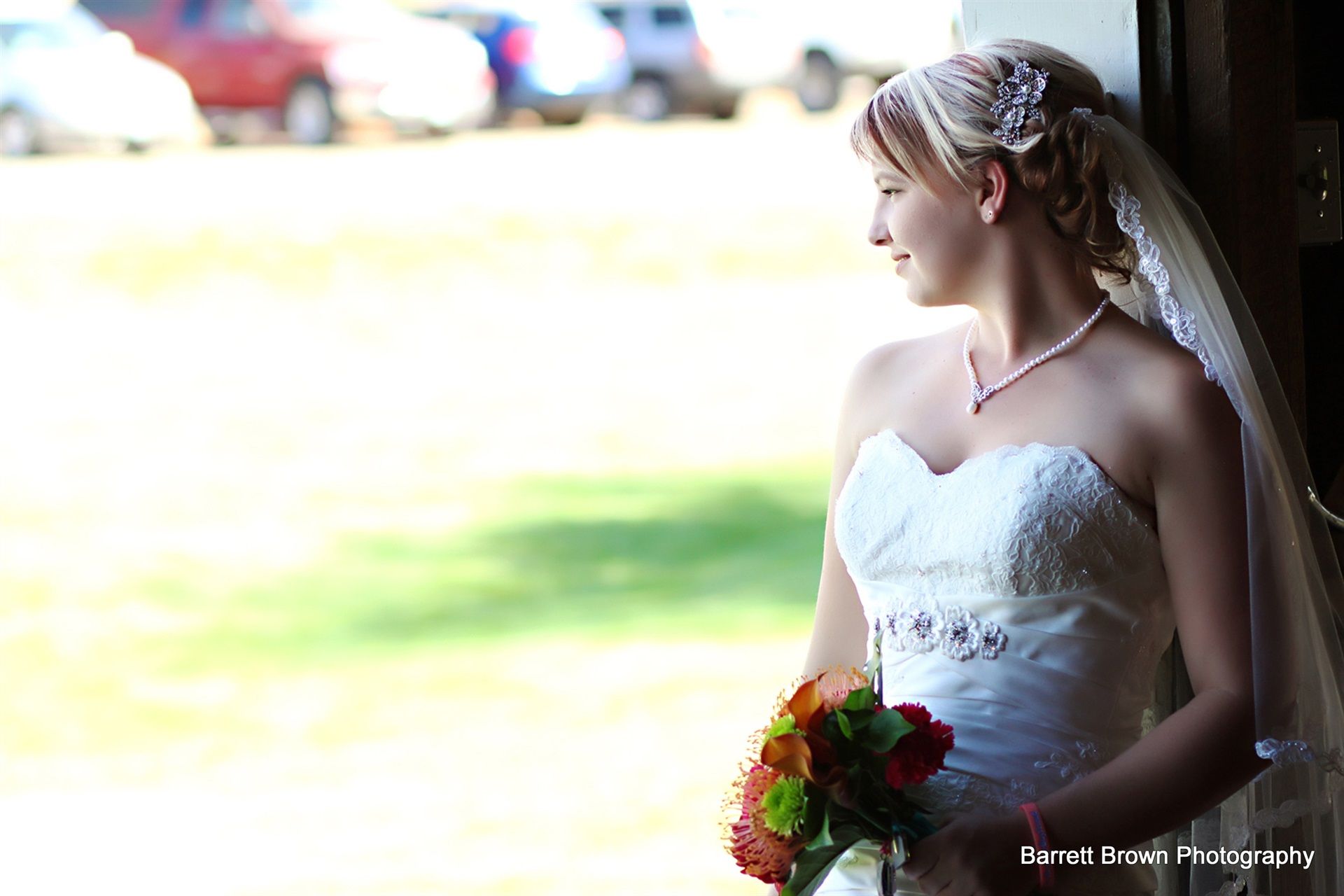 Bride, holding a red and white bouquet, looking out to blurred field