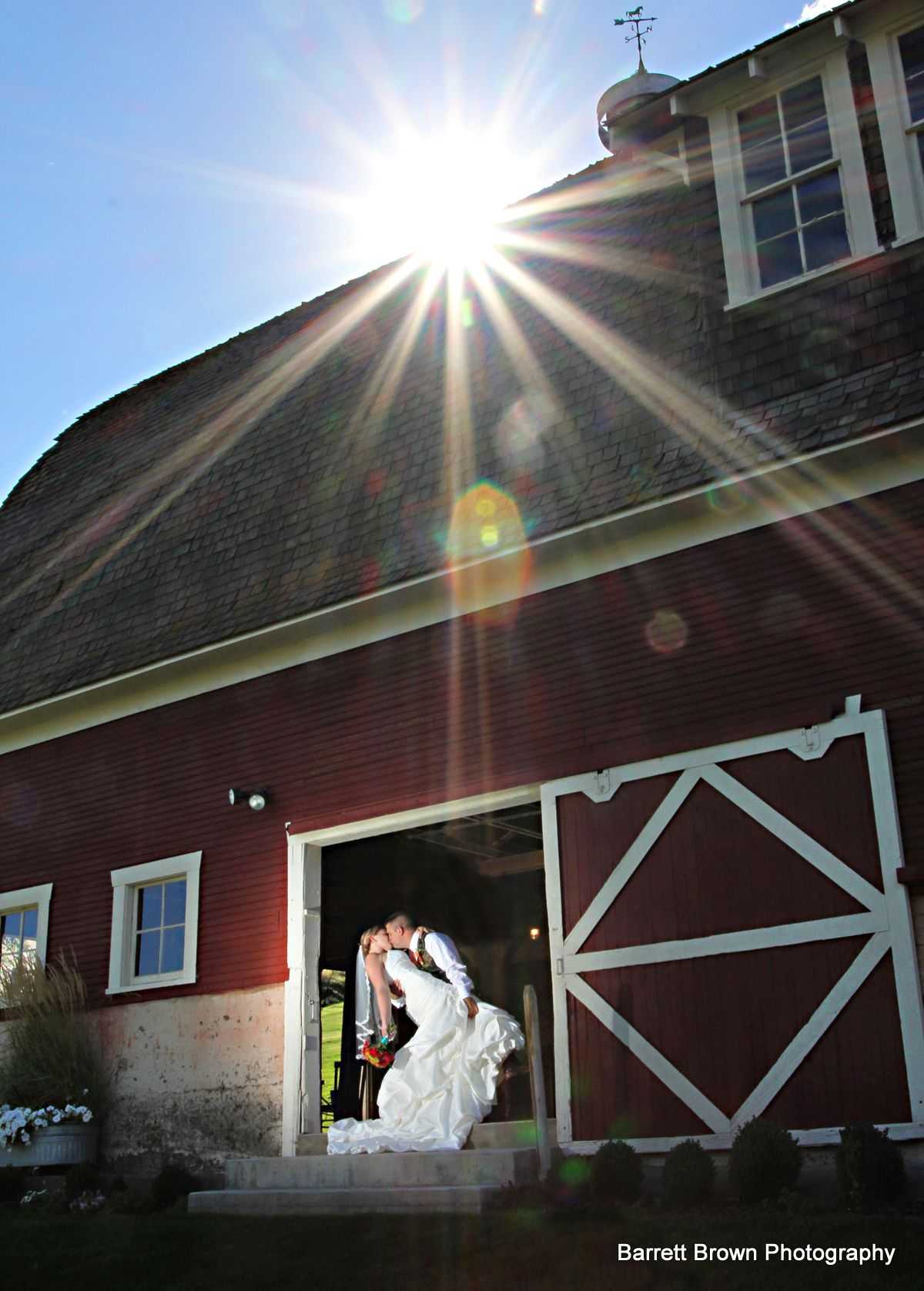 Groom dipping his bride as the couple kiss at the center of an open bar door, the sun peeking over
